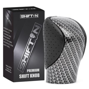 May include: Black leather and carbon fiber shift knob with a chrome accent. The knob is packaged in a black box with the text "SHIFTIN" and "PREMIUM SHIFT KNOB".