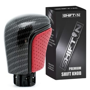 May include: A gear shift knob featuring a black carbon fiber pattern on the top and sides, with a red perforated leather-textured panel on the front. It is displayed next to a black product box labeled SHIFTN PREMIUM SHIFT KNOB.