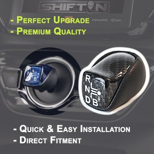 Op de afbeelding: Er worden twee autoversnellingspookknoppen getoond. E&eacute;n is zwart met witte letters en een koolstofvezelpatroon. De andere is blauw met witte letters. Tekst op de afbeelding luidt: "PERFECT UPGRADE", "PREMIUM QUALITY", "QUICK & EASY INSTALLATION" en "DIRECT FITMENT".