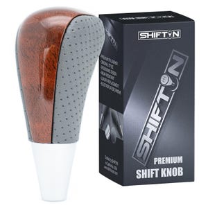 May include: A premium shift knob with a wood grain top and gray perforated grip. The base is white. The box next to it has the text "SHIFTIN" and "PREMIUM SHIFT KNOB".