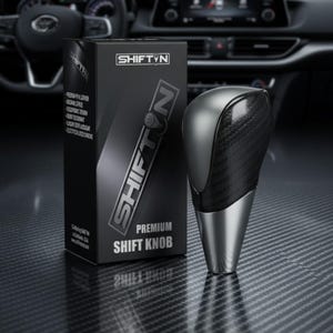 May include: A premium SHIFTYN shift knob with a carbon fiber and silver design. The black box next to it has the SHIFTYN logo and product details. The shift knob is designed for a car's gear shift.