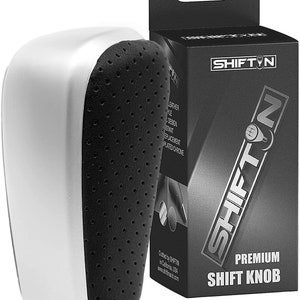 May include: A silver and black leather shift knob with a chrome accent. The knob is designed to replace the original shift knob in a car. The knob is made by SHIFTN and is crafted in California, USA.