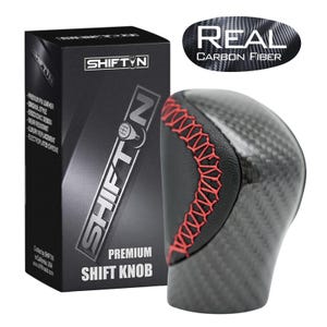 May include: A premium shift knob with a carbon fiber design and red stitching. The product is packaged in a black box with the "SHIFT N" logo and product information. The text "REAL CARBON FIBER" is also visible.