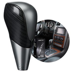 May include: A gear shift knob featuring a dark carbon fiber textured upper section and a smooth, metallic silver base. The product is displayed alongside a black box labeled SHIFTON PREMIUM SHIFT KNOB and an interior view of a vehicle dashboard.