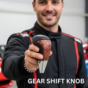 May include: Gear shift knob with a wood grain finish and a black top. The knob has a silver base and is held by a person wearing a black racing suit. The text "GEAR SHIFT KNOB" is at the bottom of the image.