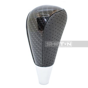 May include: A black and silver car gear shift knob with a carbon fiber pattern on the top and a perforated leather-like grip. The base is chrome, and the text "SHIFT N" is visible.