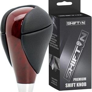 May include: A red wood and black leather car shift knob with a chrome base. The knob is packaged in a box with the brand name "SHIFT'N" and the words "Premium Shift Knob".