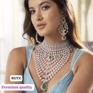 May include: A woman wearing a light blue dress with a silver and green diamond necklace and earrings. The necklace has a teardrop pendant with a green stone. The text "RUTZ Premium quality" is visible in the bottom left corner of the image.