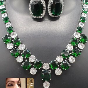 Peut inclure: Un collier et des boucles d'oreilles en argent avec de grosses pierres vert émeraude et de petites pierres claires. Le collier a un pendentif avec une grosse pierre vert émeraude.