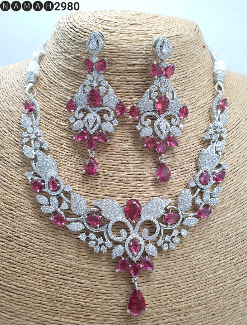 May include: A silver necklace and earrings set with a floral design and pink stones. The necklace has a pendant with a large pink stone in the center.
