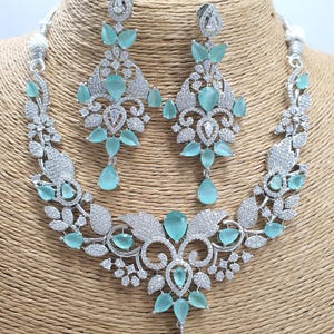 May include: A silver necklace and earrings set with a floral design and light blue stones. The necklace has a pendant with a large light blue stone.