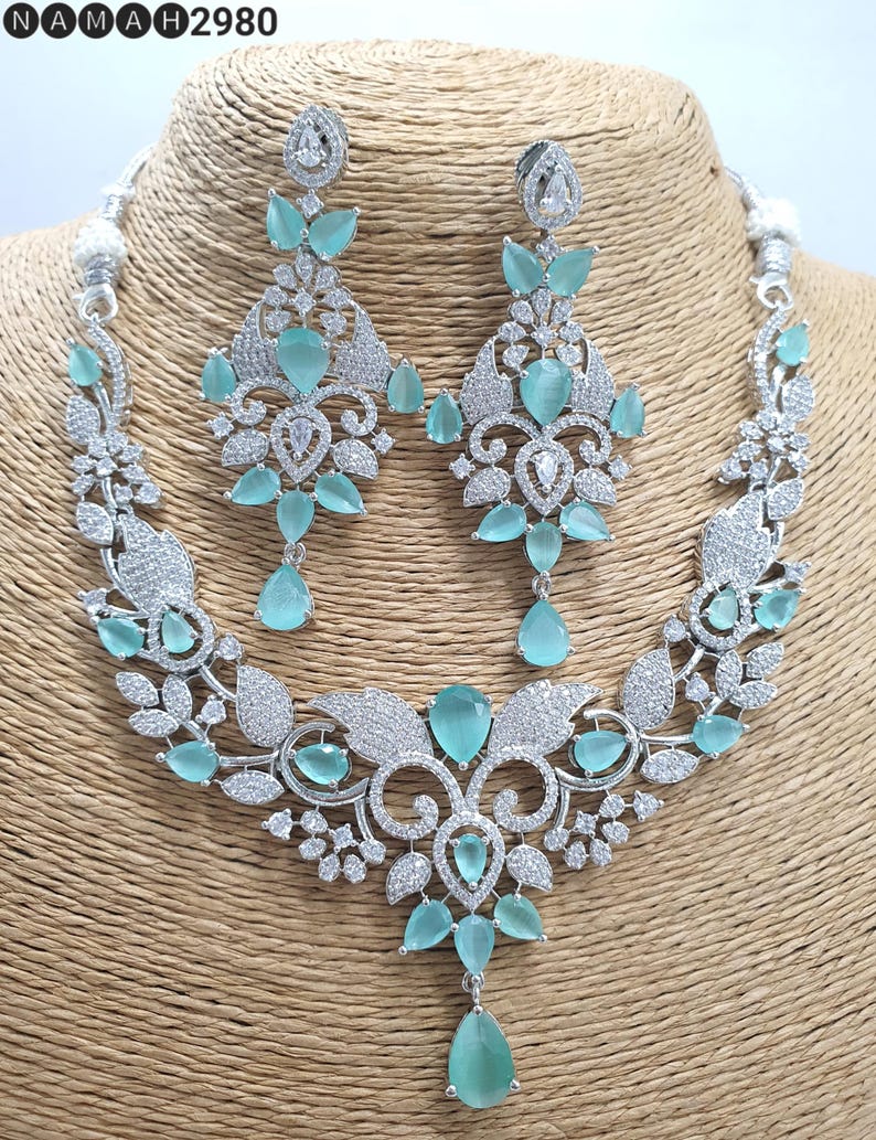 May include: A silver necklace and earrings set with a floral design and light blue stones. The necklace has a pendant with a large light blue stone.