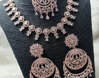 May include: A rose gold bridal jewelry set with a necklace, earrings, and a maang tikka. The set is adorned with sparkling white stones.
