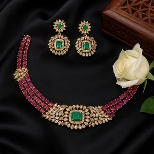 May include: A luxurious jewelry set featuring a necklace and matching earrings. The necklace has a central emerald-cut green stone, surrounded by a diamond-like halo, and is connected to three strands of small, pink stones. The earrings mirror the necklace design.
