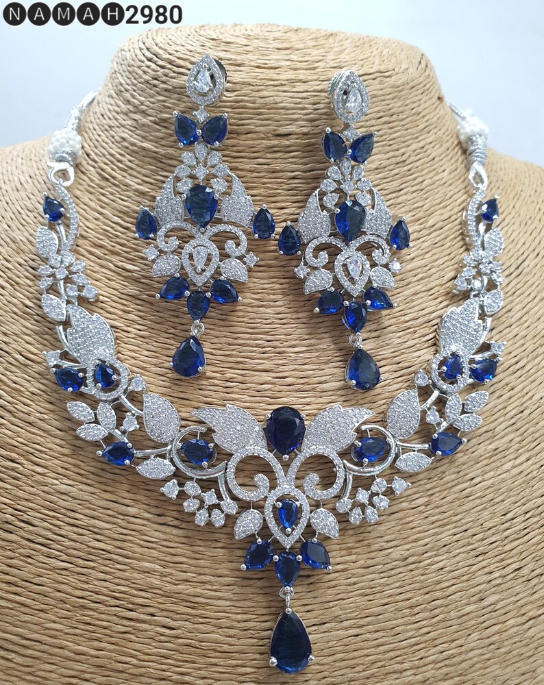May include: A silver necklace and earrings set with a floral design and blue stones. The necklace has a pendant with a large blue stone.