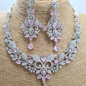May include: A silver necklace and earrings set with a floral design and pink stones. The necklace has a pendant with a teardrop-shaped stone.