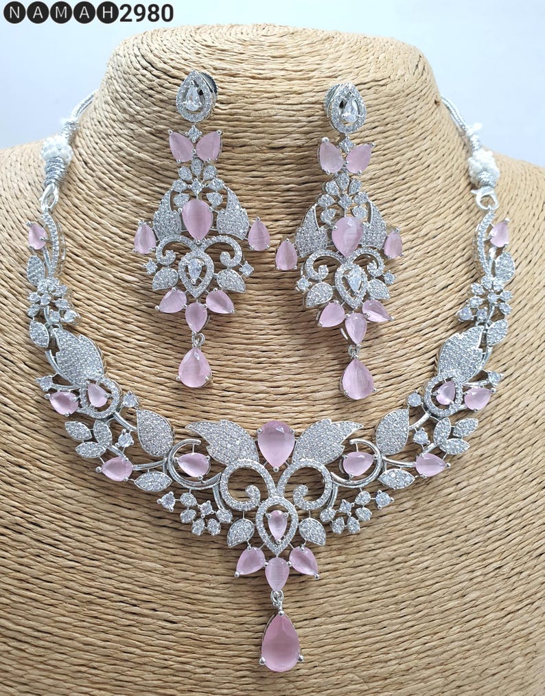 May include: A silver necklace and earrings set with a floral design and pink stones. The necklace has a pendant with a teardrop-shaped stone.