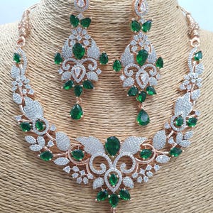 May include: A rose gold necklace and earrings set with a floral design and green and white stones.