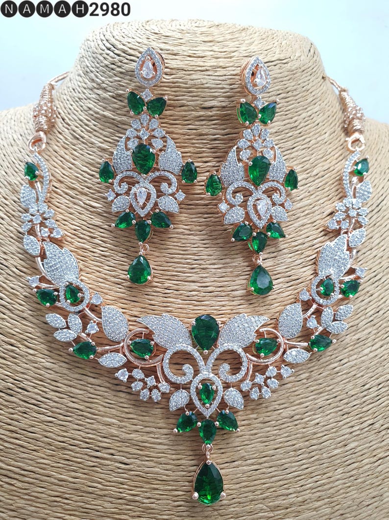 May include: A rose gold necklace and earrings set with a floral design and green and white stones.
