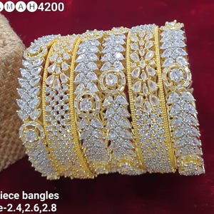 May include: Six gold bangles with white cubic zirconia stones. The bangles are stacked on top of each other and have a leaf design. The text "NAMAH4200" is visible in the top left corner of the image. The text "6 piece bangles size-2.4,2.6,2.8" is visible at the bottom of the image.