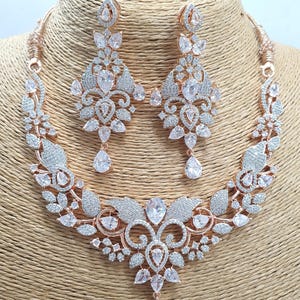 May include: A rose gold necklace and earrings set with a floral design and clear cubic zirconia stones.