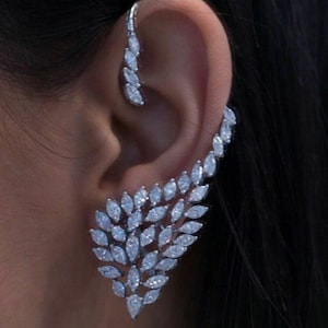Puede incluir: Un pendiente de aro de plata con un diseño en cascada de piedras de circonita cúbica transparentes. Las piedras están dispuestas en forma de hojas, creando un look delicado y elegante.