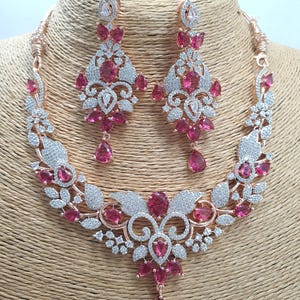 May include: A rose gold necklace and earrings set with a floral design and pink stones. The necklace has a pendant with a teardrop-shaped stone.