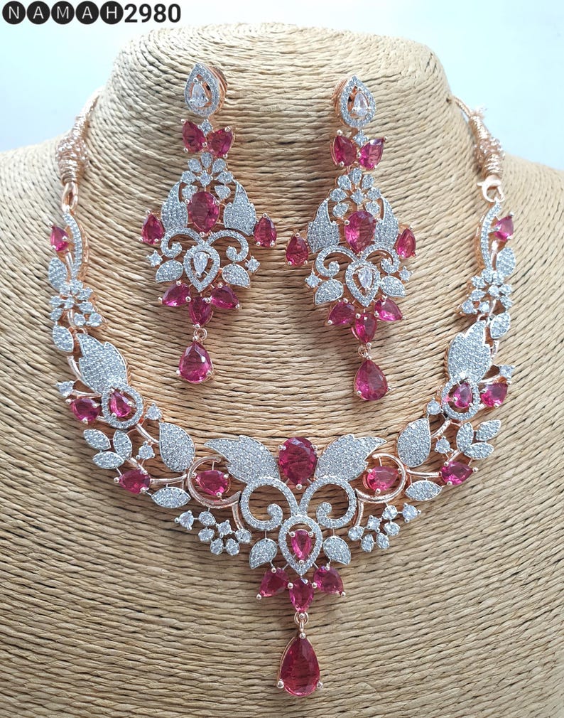 May include: A rose gold necklace and earrings set with a floral design and pink stones. The necklace has a pendant with a teardrop-shaped stone.