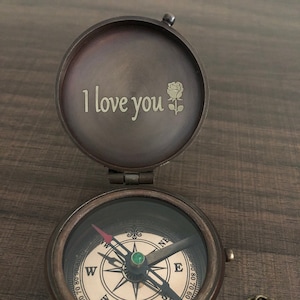 May include: A brass compass with a chain, the lid is open and engraved with the words "I love you" and a rose.