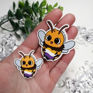 May include: Two bee-themed stickers with the text "Bee Yourself" on each. The larger sticker features a yellow and black bee with a purple, white and yellow heart. The smaller sticker is the same design but smaller.