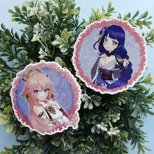 Peut inclure: Deux autocollants de personnages de style anime avec des accents roses et bleus. Les autocollants sont ronds et présentent un personnage aux cheveux roses avec une tenue blanche et un personnage aux cheveux bleus avec une tenue violette et blanche.