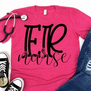 May include: A hot pink t-shirt with the words "ER Nurse" in black script. A black stethoscope rests on the shirt. The shirt is paired with blue jeans and black and white sneakers.