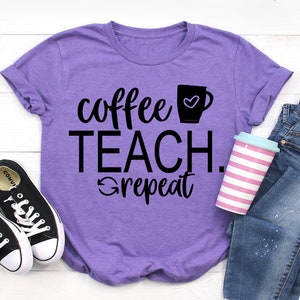 以下が含まれることがあります： コーヒーカップにハートマークが描かれた黒い文字で「coffee teach. repeat」と書かれた紫色のTシャツです。