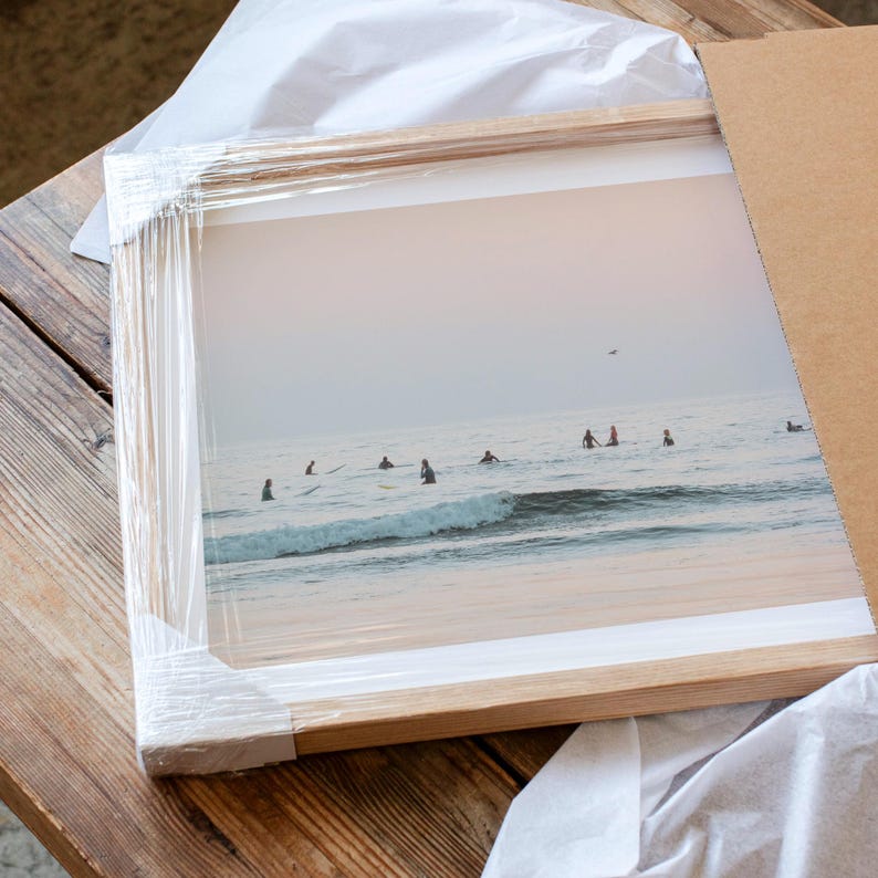 a framed photograph of people surfing on a beach, with the ocean and sky visible in the background.