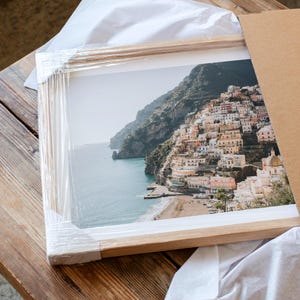 A framed photograph of a picturesque coastal town nestled on a cliff overlooking the sea, with colorful buildings and a sandy beach.