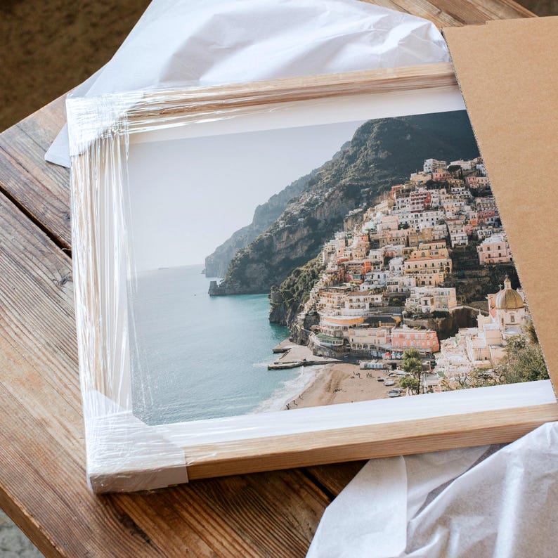 A framed photograph of a picturesque coastal town nestled on a cliff overlooking the sea, with colorful buildings and a sandy beach.