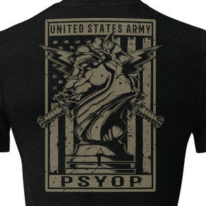May include: A black short-sleeve t-shirt featuring a graphic on the back. The design includes a stylized horse head, two crossed swords, and a flag background with the text UNITED STATES ARMY and PSYOP in a rectangular frame in tan and black.