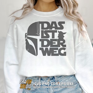 May include: White sweatshirt with a gray graphic design featuring a helmet, a character, and the German phrase "DAS IST DER WEG." The bottom of the sweatshirt shows the text "GRAFIX STUDIO" and "SVG PNG CDR EPS DXF".