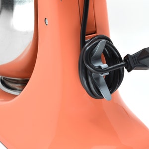 May include: A coral orange stand mixer with a silver bowl and a black cord wrapped around the base.