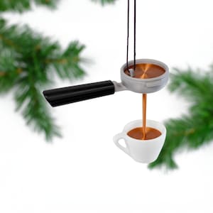 Może przedstawiać: Ozdoba w kształcie srebrnej i czarnej ekspres do kawy z brązowym kubkiem. Ekspres wlewa kawę do kubka.