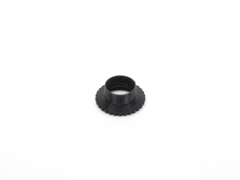May include: A black plastic ring with a ridged outer edge. The ring is designed to be used as a camera lens adapter.