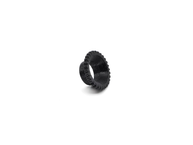 May include: Black plastic ring with a textured, gear-like design. The ring is about 1 inch in diameter.
