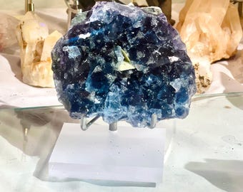 May include: A large blue and purple fluorite crystal with a white crystal inside. The crystal is on a clear acrylic stand.