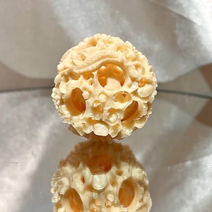 May include: A carved ivory ball with intricate designs and openwork. The ball is a light cream color and has a smooth, polished finish.