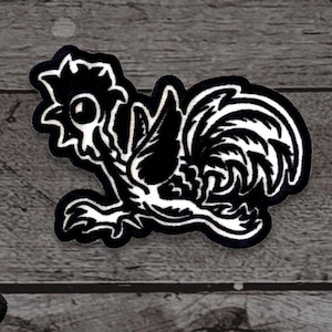 May include: A black and white embroidered patch featuring a stylized rooster design. The rooster is depicted in a side profile with detailed feathers and a prominent comb. The patch has a black border and is likely for clothing or accessories.