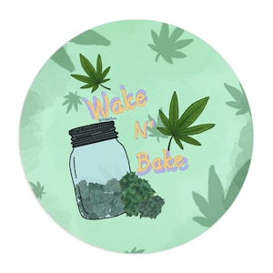 May include: Round sticker with a light green background and cannabis leaf silhouettes. A jar filled with green buds and the words "Wake N' Bake" in colorful text are featured. The sticker has a playful, illustrative style.
