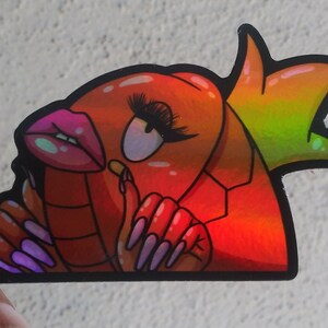 Puede incluir: Una pegatina hologr&aacute;fica de una langosta de dibujos animados con u&ntilde;as largas de color rosa, pintalabios y una corona. La langosta es roja y naranja con un contorno negro.