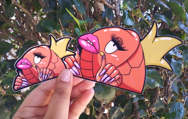 Puede incluir: Dos pegatinas de peces de dibujos animados de color rojo y naranja con coronas amarillas y u&ntilde;as largas de color rosa y morado. Los peces tienen ojos grandes y labios rosas.