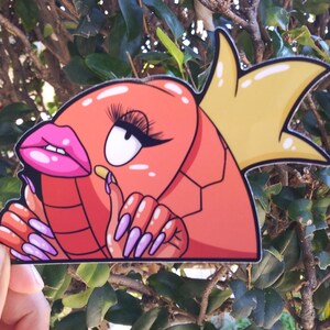Puede incluir: Una pegatina de dibujos animados roja y amarilla de un personaje con pesta&ntilde;as largas, labios rosados y u&ntilde;as largas. El personaje lleva una corona.