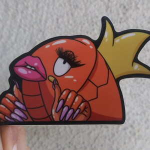 Puede incluir: Un langostino de dibujos animados rojo y naranja con u&ntilde;as largas de color p&uacute;rpura y una corona amarilla. El langostino lleva maquillaje y tiene una boca rosa de puchero.